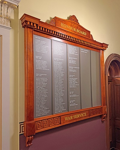 Wooden honour board on a wall, titled “Honour Board” and “War Service,” listing names of people who served in wars.
